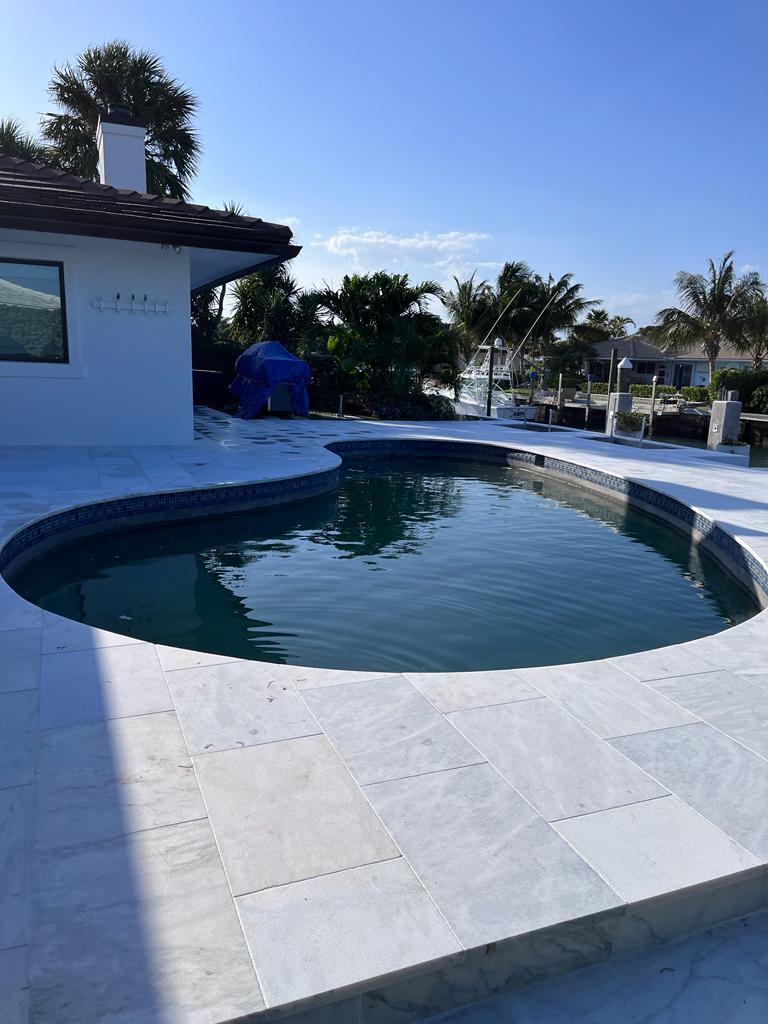 A curved swimming pool surrounded by white porcelain pavers